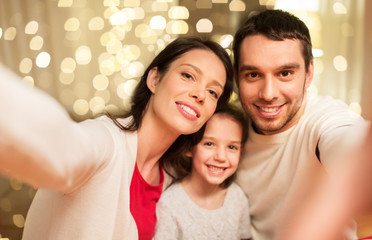 family, christmas and holidays concept - happy mother, father and little daughter taking selfie at home