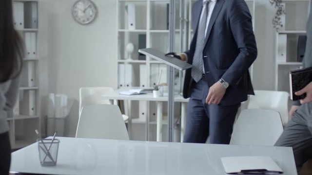 Caucasian businessman with prosthetic hand walking with colleagues into office, sitting at table, opening laptop and starting corporate meeting