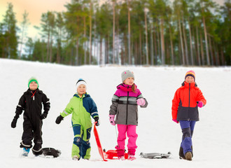 childhood, sledging and season concept - group of happy little kids with sleds in winter over forest background