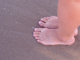 Closeup Female feet with pedicure on a beach sand. View from above