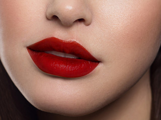 Beauty closeup of women full red lips with shiny skin and long hair. Facial skin care in a spa salon or cosmetology and a fashionable red lip gloss. Evening makeup