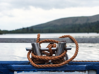 A coil of orange rope around cleats on the stern of a blue wooden boat.
