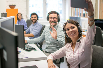 Beautiful woman customer support operator taking a selfie photo of her team colleagues in a call...