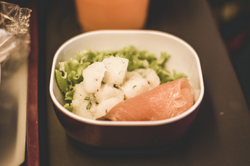 airline inflight economy class meal served on a tray with potato salad, smoked salmon and lettuce with orange juice in the background