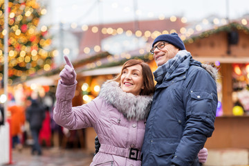 travel, tourism, holidays and people concept - happy senior couple hugging at christmas market on...