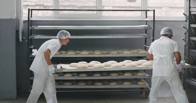 Raw bread load from the shelf in the industrial oven machine in a big bakery industry, the main baker walked around in a special beautiful uniform , other worker with shelves transported the fresh