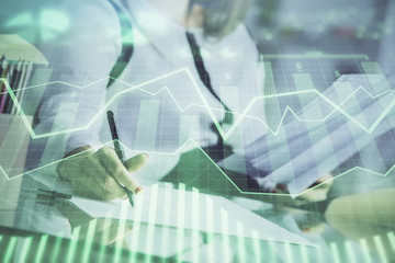A woman hands writing information about stock market in notepad. Forex chart holograms in front. Concept of research.