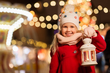 holidays, childhood and people concept - happy little girl with lantern at christmas market in...
