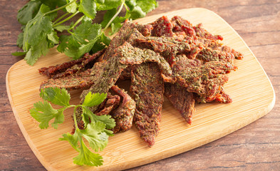 A Pile of Gourmet Cilantro Flavored Beef Jerky on a Wooden Cutting Board