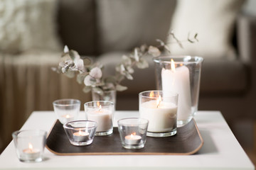 decoration, hygge and cosiness concept - burning white fragrance candles on tray and branches of eucalyptus populus on table at cozy home