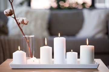 decoration, hygge and cosiness concept - burning white candles and cotton flower branch on table at...