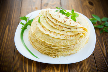 many fried thin pancakes in a plate, on a table.