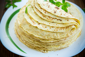 many fried thin pancakes in a plate, on a table.