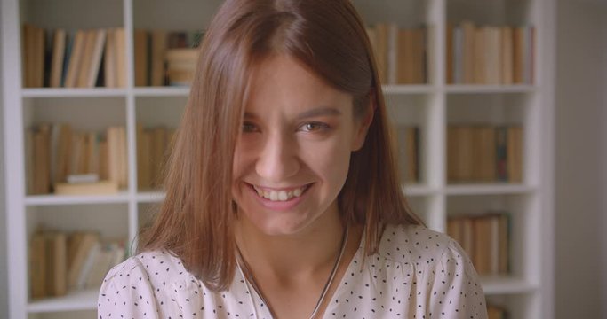 Closeup portrait of young pretty caucasian female student looking at camera laughing happily in library indoors