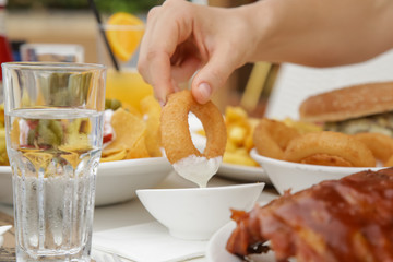 Closeup of female hand dipping fried onion ring in white garlic sauce