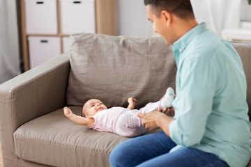 family, parenthood and fatherhood concept - middle aged father playing with little baby daughter lying on sofa at home