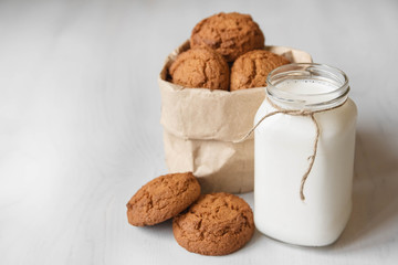 Milk in a glass jar and oatmeal cookies in a paper bag on a white table background. Copy, empty space for text