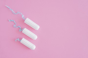 Three hygienic tampons on a pink background. Menstrual mothly cycle, means of protection. Top view, flat lay, copy space for text.