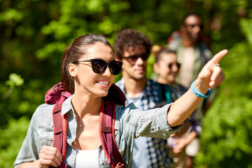 travel, tourism, hike and people concept - woman showing something to group of friends walking with...