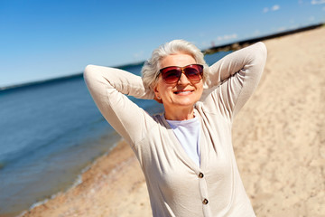 people and leisure concept - portrait of happy senior woman in sunglasses on beach in estonia