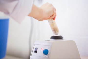 The laboratory scientist mixes the biological sample for analysis on lab vortex mixer with adjustable stirring speed with touch.