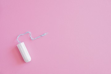 One hygienic tampon on a pink background. Menstrual mothly cycle, means of protection. Top view, flat lay, copy space for text.