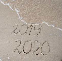 New Years 2020 replace 2019 concept. End of 2019 Happy New Year 2020, lettering on beach with wave and clear blue sea. Handwritten inscription 2019 and 2020 on beautiful sand beach.