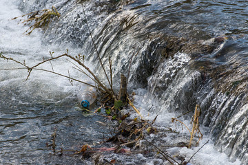 Floating plastic bottle in the clean small river, conceptual image of human negligence.