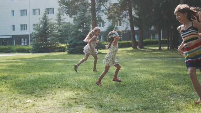 children run after each other in the summer park. blindfolded girl catches her friends.