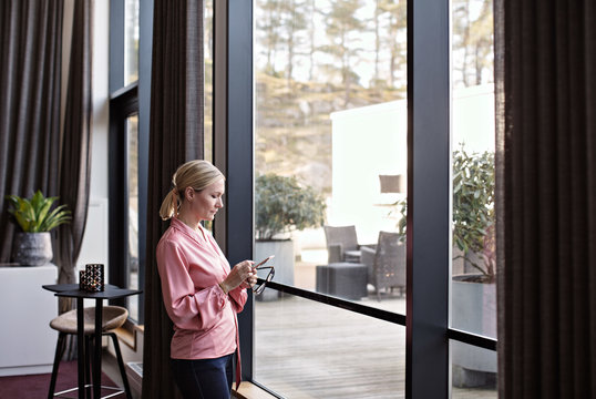 Businesswoman using phone while standing by window in office