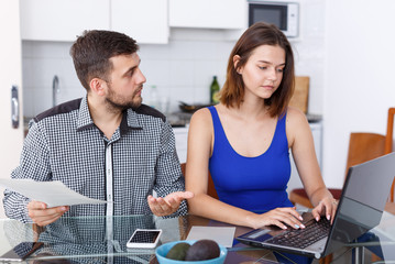 Serious young man and woman with financial documents near laptop