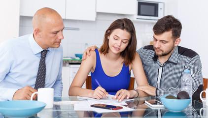 Smiling young man and wife signing agreement papers with social worker