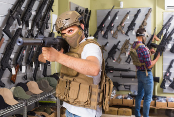 Young guys in military equipment with rifle in airsoft shop
