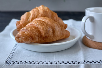 Fresh backed French croissants and cup of coffee on black table and white napkin. Continental breakfast. Close up