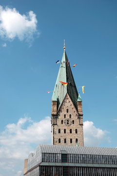 Der Hohe Dom St. Maria, St. Liborius, St. Kilian mit bunten Fahnen am Kirchturm im Sommer vor blauem Himmel mit wei&szlig;en Wolken im Sonnenschein im Bistum Paderborn in Ostwestfalen-Lippe