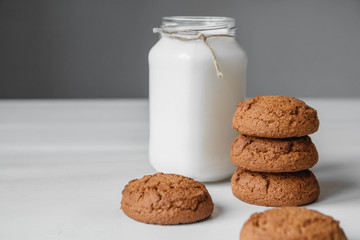 Milk in a glass jar and oatmeal cookies on a white table background. Copy, empty space for text