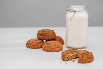 Milk in a glass jar and oatmeal cookies on a white table background. Copy, empty space for text