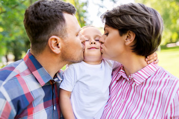 Fototapeta premium family, leisure and people concept - happy mother and father kissing their little son at summer park