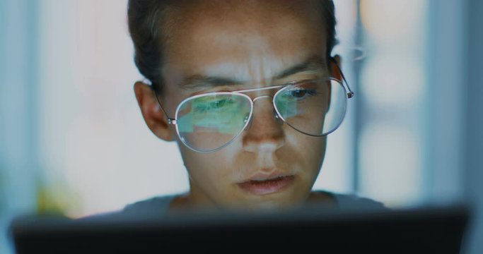 High quality 4k 12bit footage. Young office worker in glasses typeing on a laptop, figuring out problems. late-night work. Woman at the computer is looking for a solution to the problem.