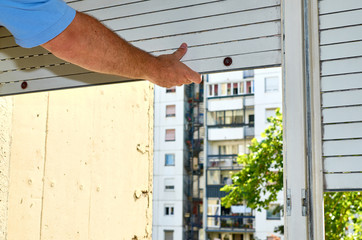 Hand holding a blind while fixing a stacked part of it with a residential building in a background
