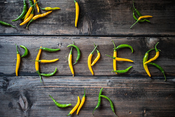 Word PEPPER made of raw organic yellow and green chili cayenne peppers on old wooden table