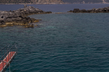 Part of the yacht ladder, blue sea, on the horizon - rocks