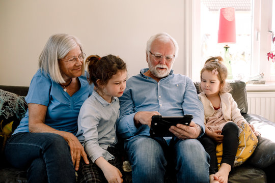 Grandparents sitting with grandchildren while using digital tablet at home