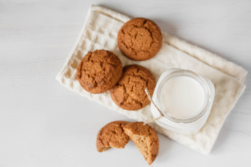 Milk in glass jar and oatmeal cookies near napkin on white table background. Top view. Copy, empty space for text
