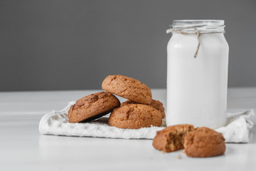 Milk in glass jar and oatmeal cookies near napkin on white table background. Copy, empty space for text