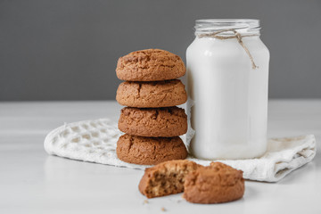 Milk in glass jar and oatmeal cookies near napkin on white table background. Copy, empty space for text