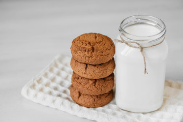 Milk in glass jar and oatmeal cookies near napkin on white table background. Copy, empty space for text