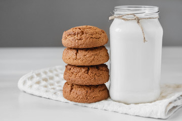 Milk in glass jar and oatmeal cookies near napkin on white table background. Copy, empty space for text