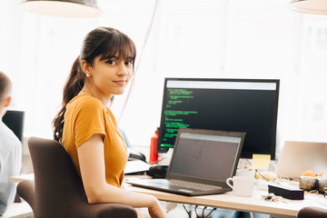 Portrait of female programmer using laptop while sitting at desk in office