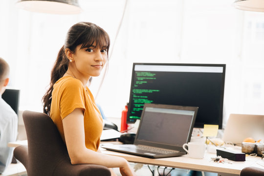 Portrait of female programmer using laptop while sitting at desk in office